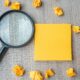 empty-yellow-note-with-crumbled-paper-and-magnifying-glass-on-wo